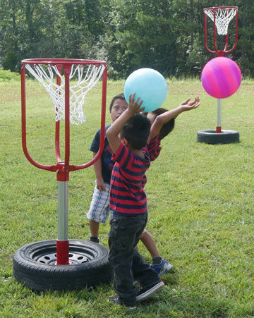 Two children playing with colorful balls near portable basketball hoops with tire bases on grass