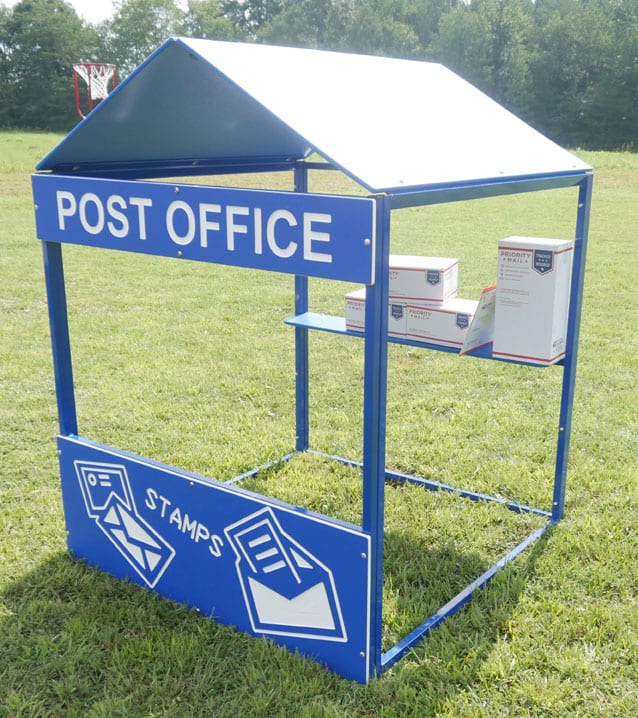 Blue metal playhouse with "Post Office" sign, stamp graphics, and play mail packages on grass