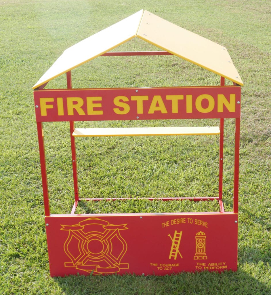 Red and yellow outdoor fire station playhouse with firefighter emblem and themed graphics on grass