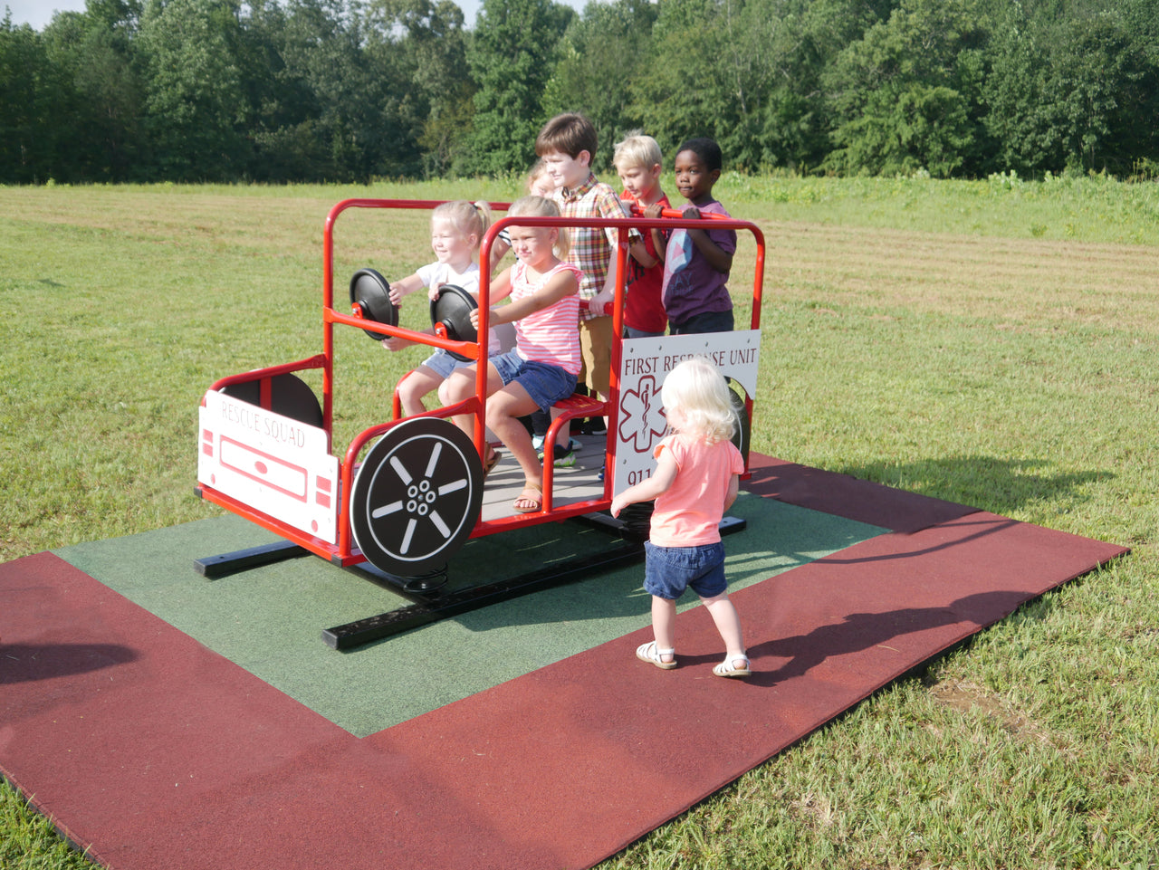 Red metal rescue truck spring rider with multiple steering wheels and children playing on safety mat outdoors