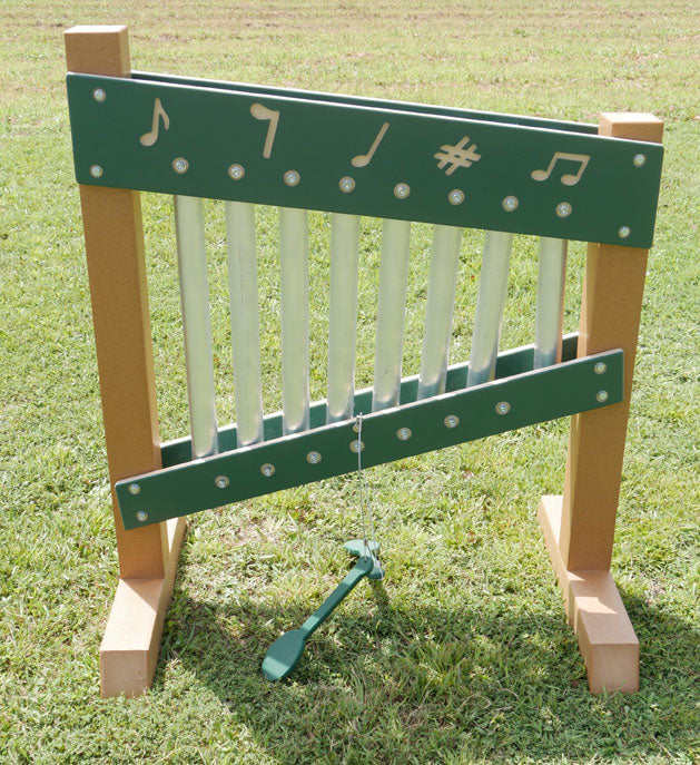 Outdoor freestanding musical chime wall with metal tubes and green panels featuring musical note symbols on grass