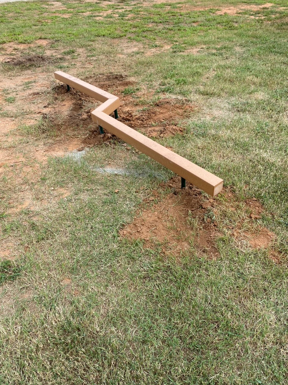 Low-profile zigzag balance beam made of recycled plastic lumber on grassy outdoor fitness area