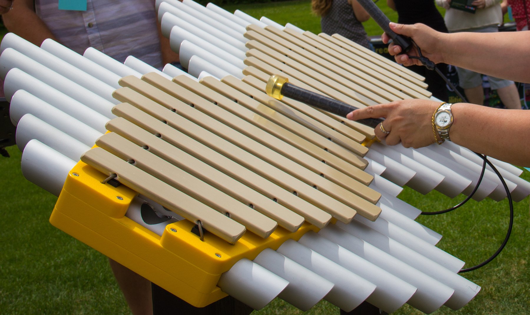 Imbarimba Outdoor Musical Park Instrument with yellow frame, beige pentatonic fiberglass bars, white resonator tubes, and attached mallets in outdoor setting