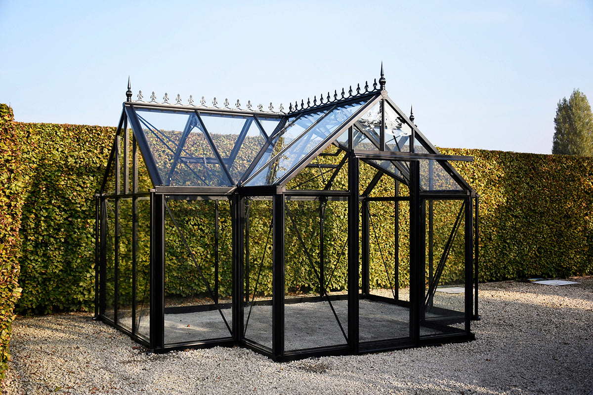 Black-framed glass greenhouse with decorative roof cresting, automatic vents, sliding door, and gravel base