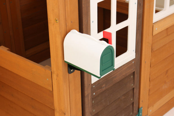 White and green wall-mounted mailbox with red flag attached to wooden playset panel of outdoor kids' swing set