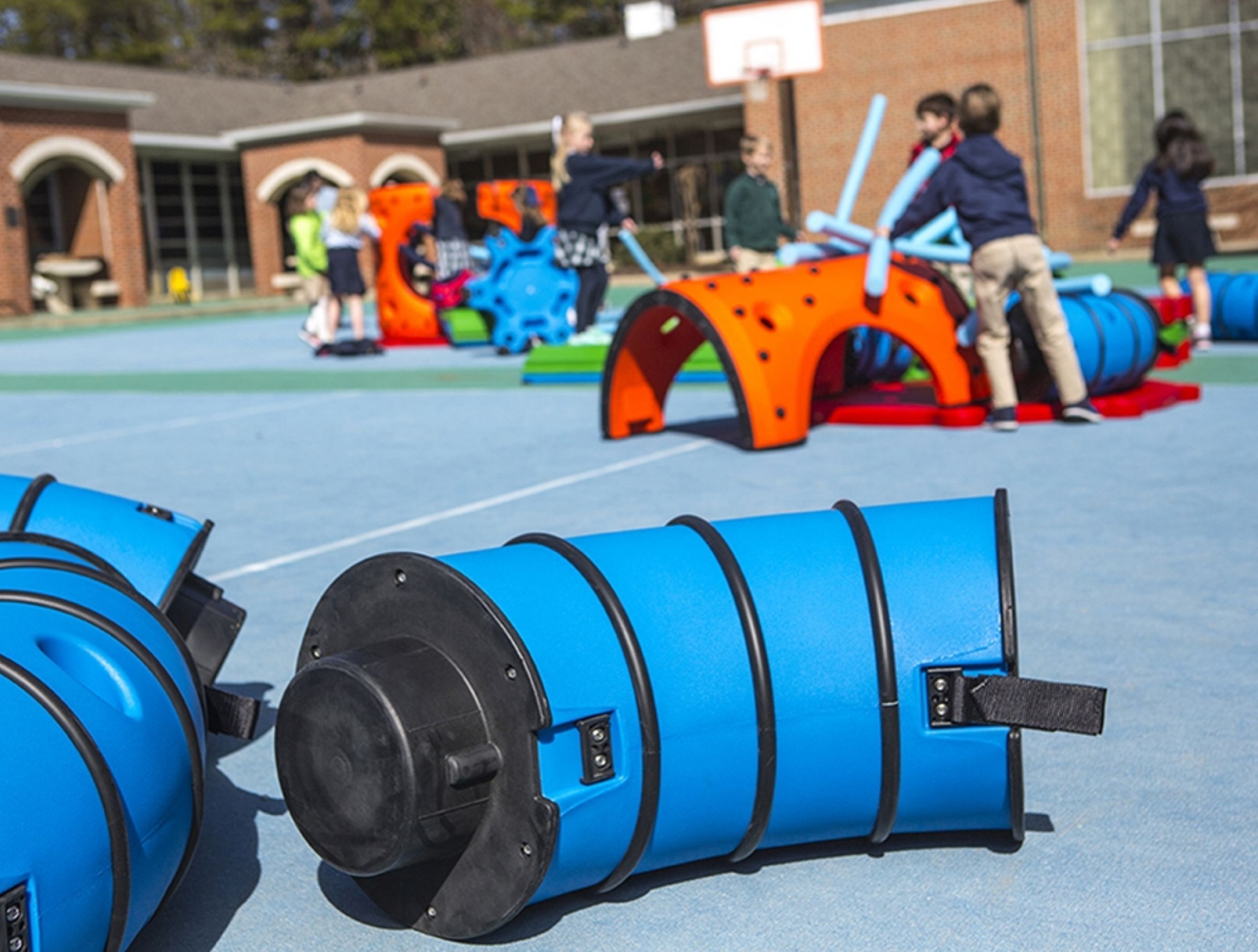 Outdoor playground with blue tunnel sections and orange climbing structures, children actively playing and exploring.