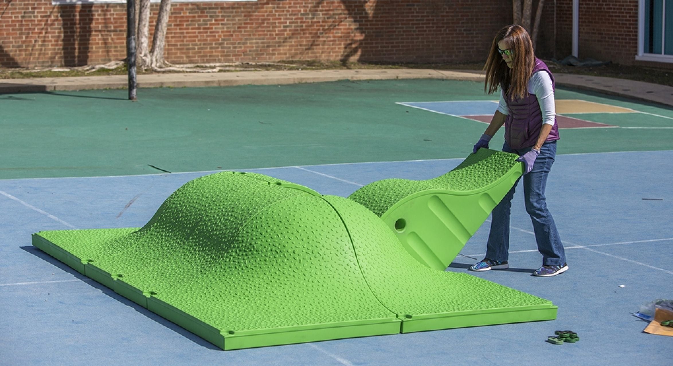Bright green textured modular play equipment on outdoor sports court for interactive physical and cognitive play