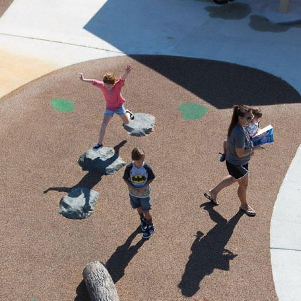 Overhead view of three hand-painted, naturalistic stepping boulders on playground surface with children climbing nearby