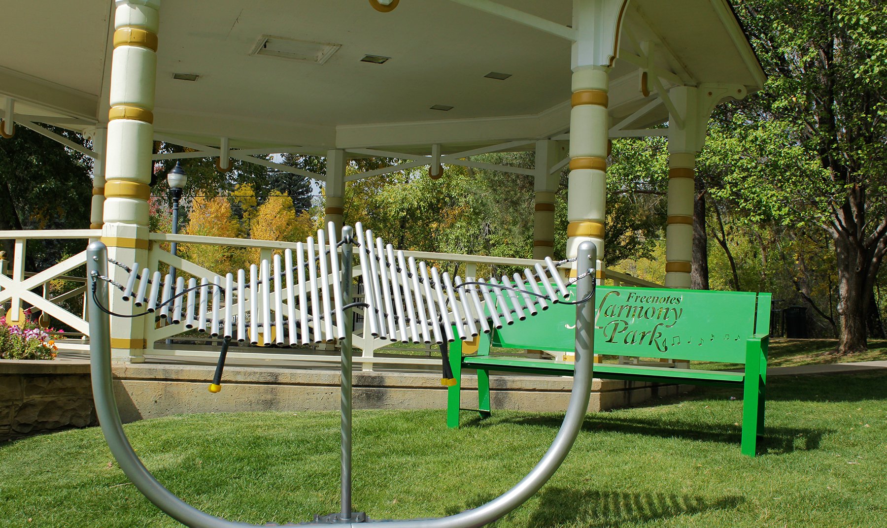 Outdoor metallophone with curved steel frame and suspended chime tubes in a park setting
