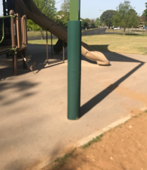 Green wrap-around safety pole pad on square playground pole near slide in outdoor play area