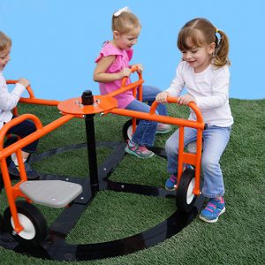 Children riding an orange self-propelled merry-go-round with seats and handlebars on artificial grass
