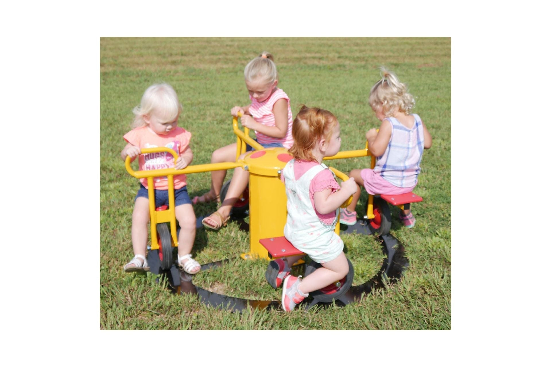 Four toddlers seated on a colorful yellow and red four-seat inground merry-go-round play rider on grass