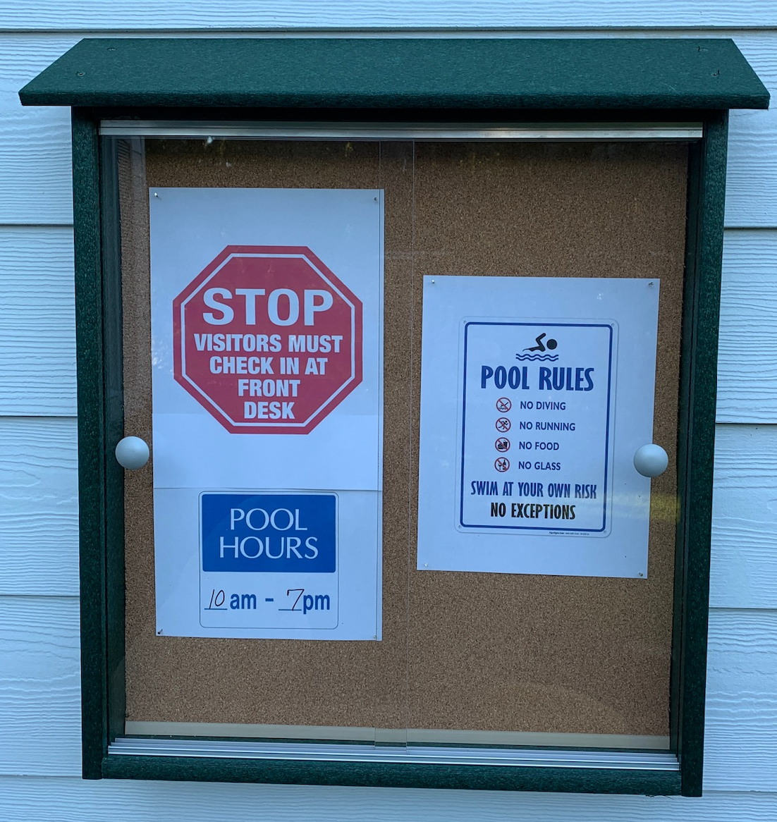 Green-framed outdoor cork bulletin board with sliding glass doors displaying pool rules and visitor check-in notices