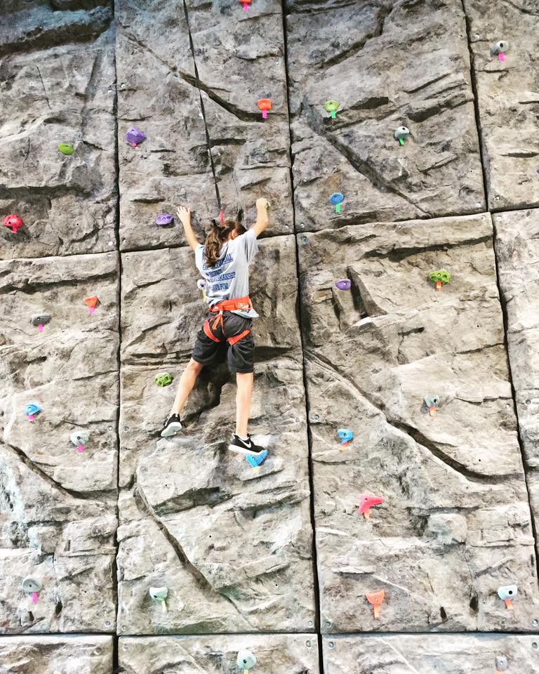 Child climbing on colorful handholds attached to a textured, rock-like modular climbing panel for outdoor play.
