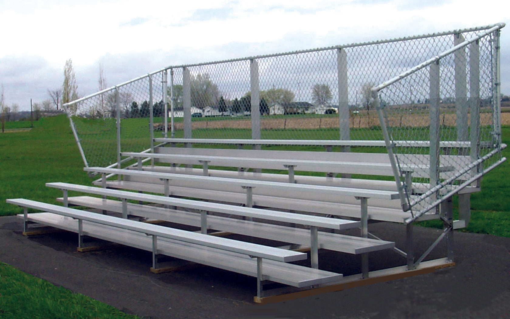 Five-row aluminum bleachers with anodized seating planks and chain-link guardrail on outdoor asphalt sports venue