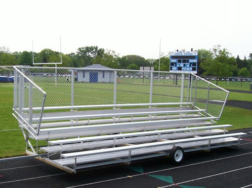 Five-row portable aluminum bleachers with chain-link guardrail on wheels, positioned on a sports field track.