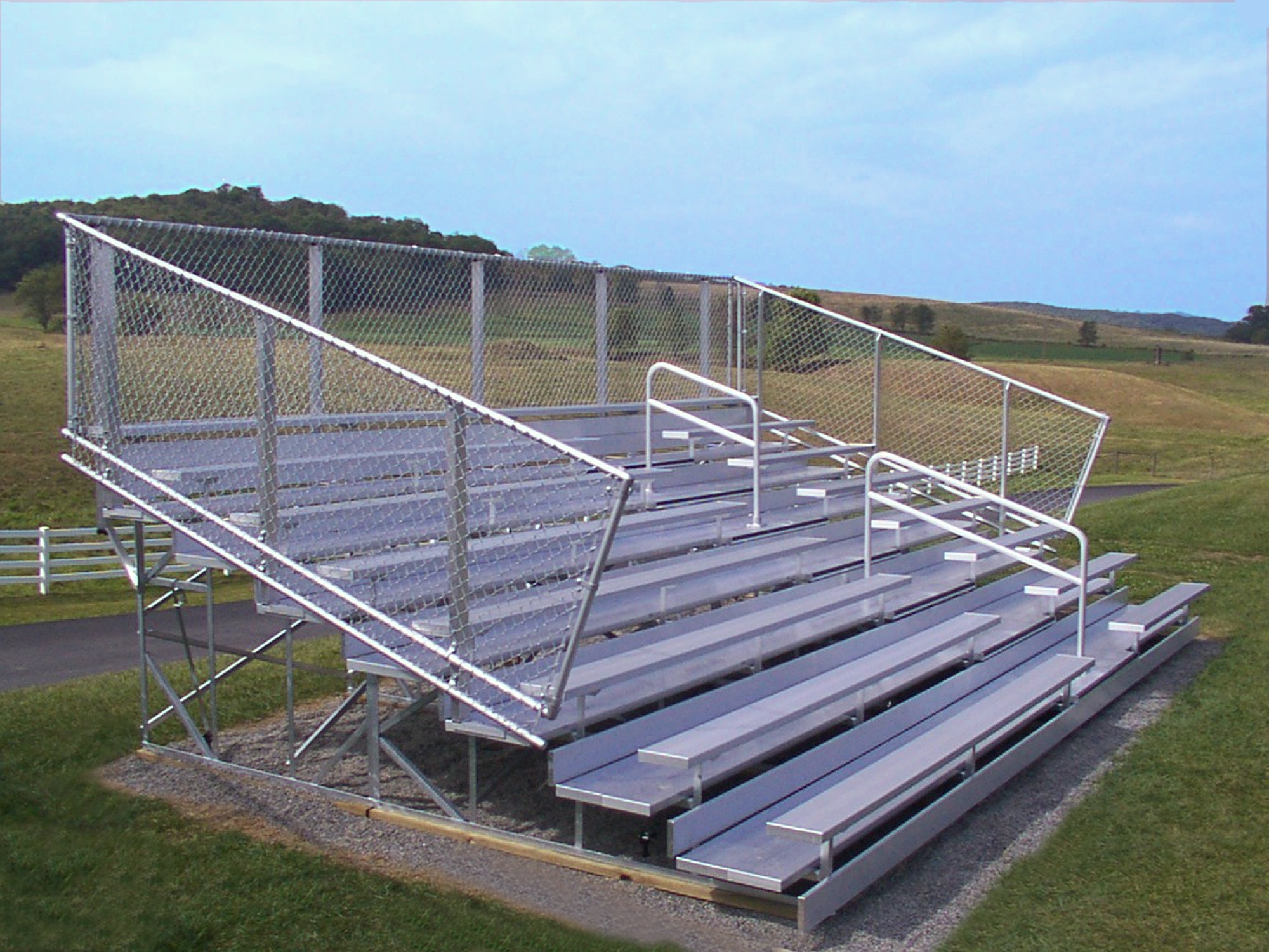 8 Row Deluxe Bleachers with aluminum seating, chain-link guardrails, and aisle handrails in outdoor sports field setting