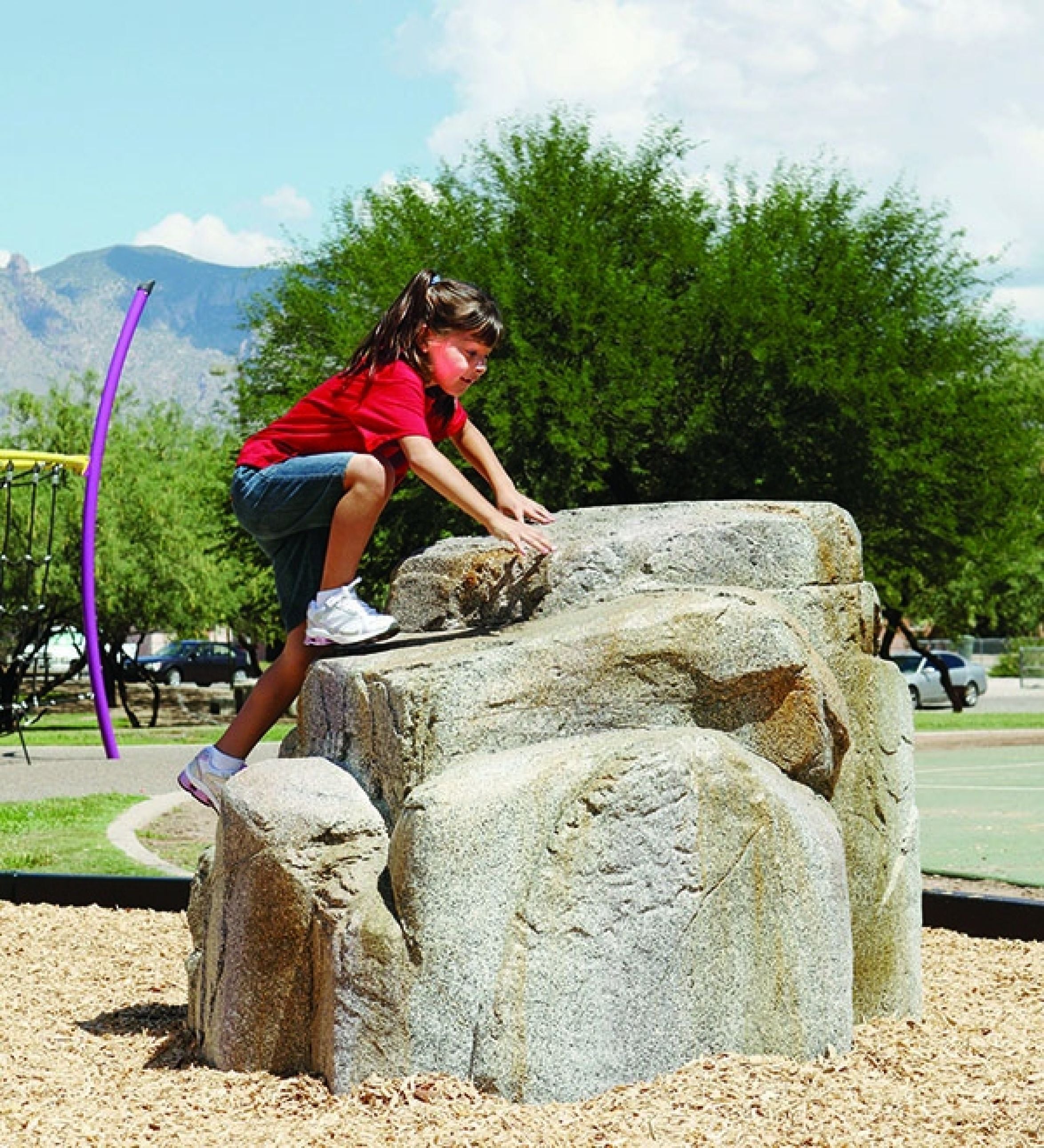 Child climbing on textured, hand-painted granite-style climbing boulder in outdoor playground setting
