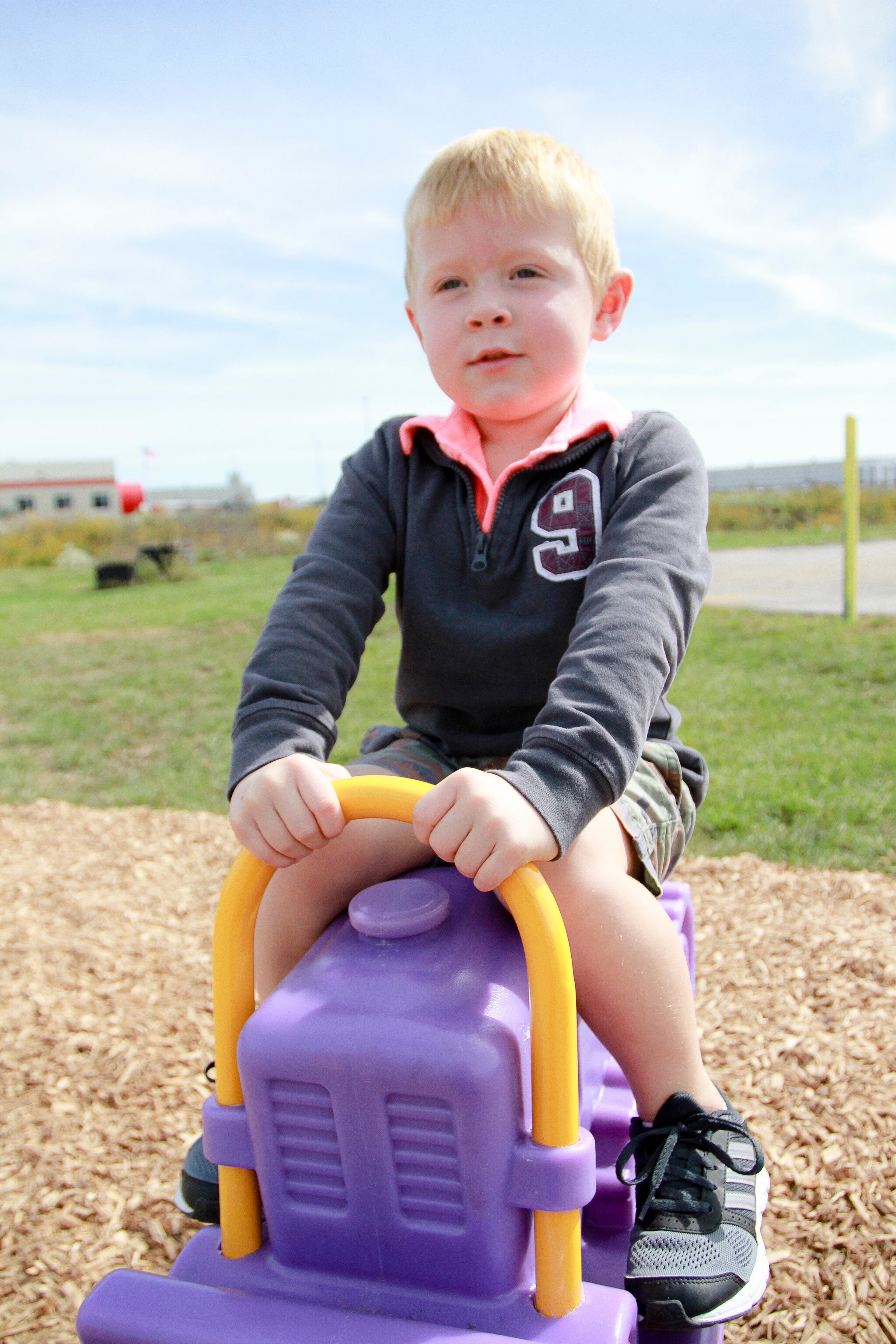 Young child on a purple and yellow bulldozer-shaped playground spring rider on wood chip surface outdoors