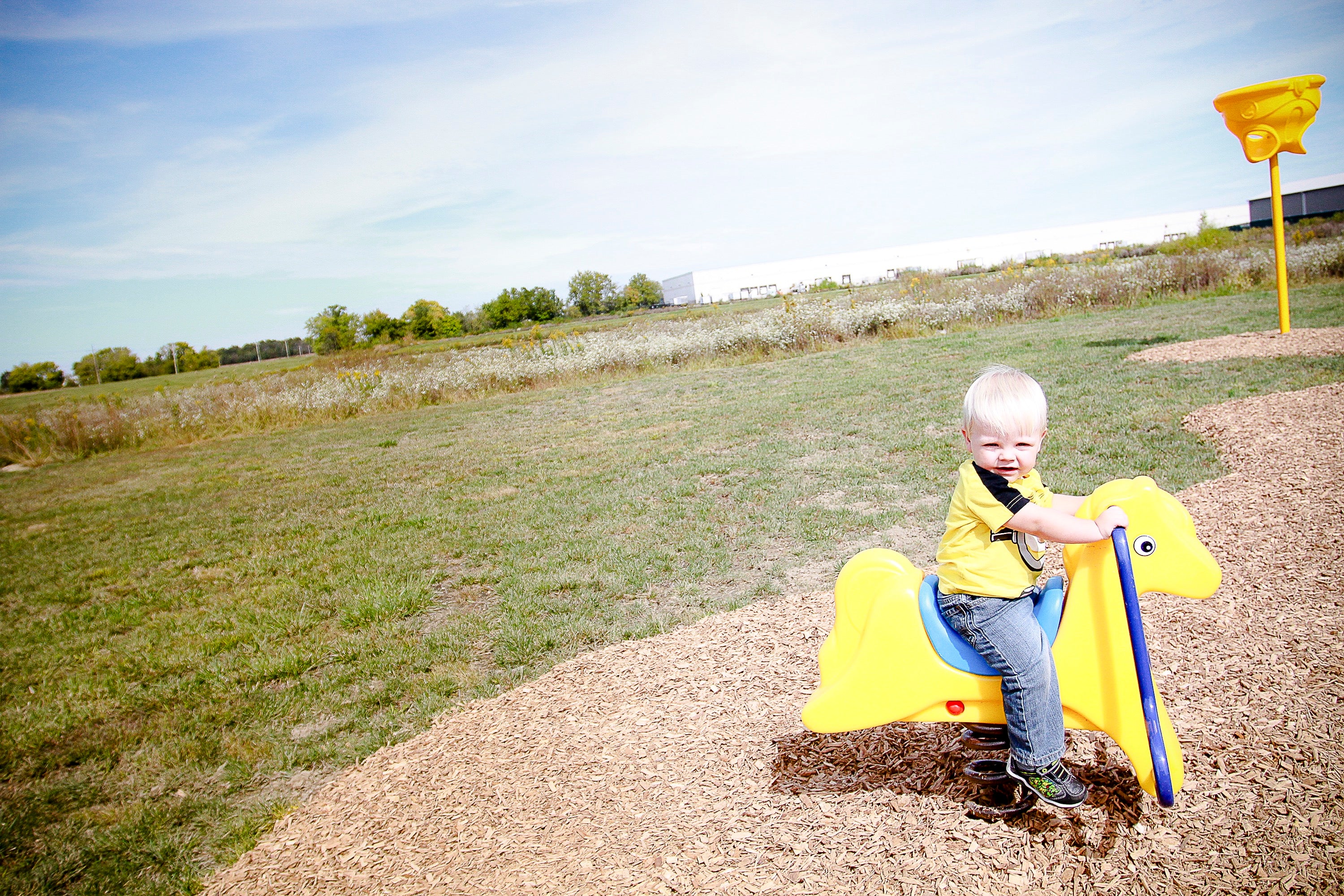 Young child seated on bright yellow pony spring rider playground equipment on wood chip surface outdoors
