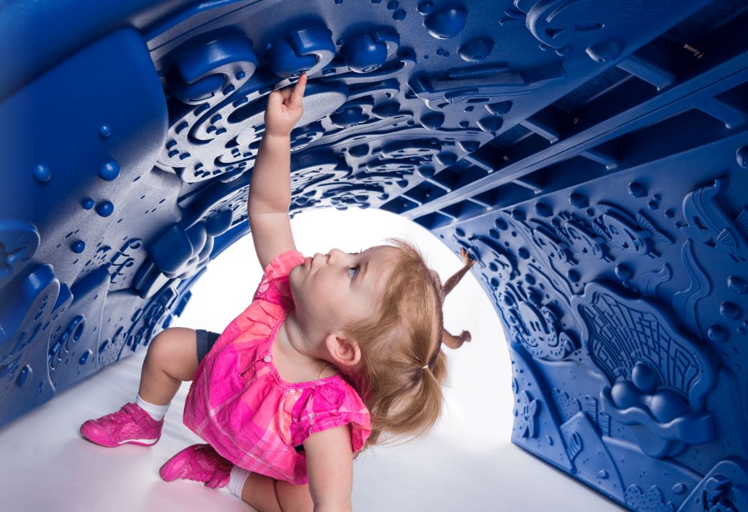 Toddler inside a blue underwater-themed play tunnel with embossed ocean creatures and symbols