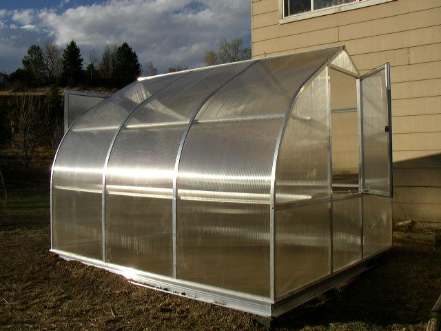 Riga 3s Greenhouse with curved twin-wall polycarbonate panels, barn-style door with lock, roof window, and rear wall window in outdoor setting