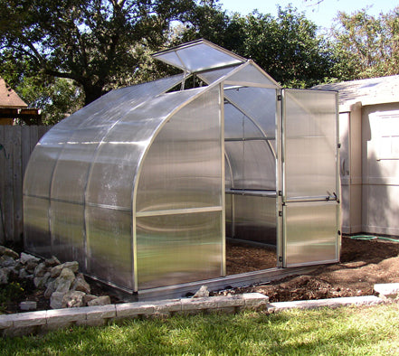 Curved polycarbonate greenhouse with automatic roof vent, barn-style door with lock, and large rear wall window in garden setting