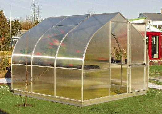 Curved twin-wall polycarbonate greenhouse with barn-style door, roof and rear windows, and plants inside on grass.
