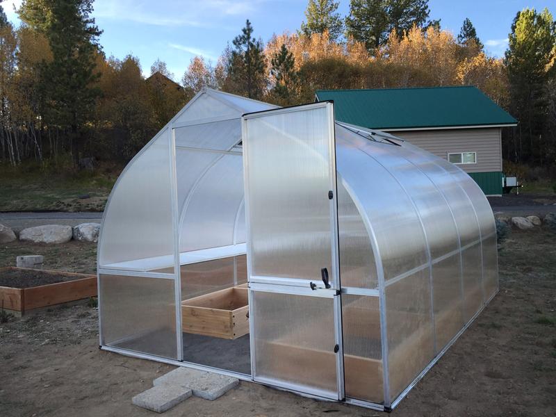 Curved greenhouse with 8mm twin-wall polycarbonate panels, barn-style door, roof vents, and wooden planting beds inside.