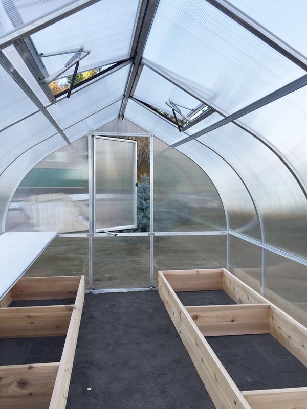 Polycarbonate greenhouse interior with raised wooden beds, twin-wall panels, roof vents, and barn-style door with lock.