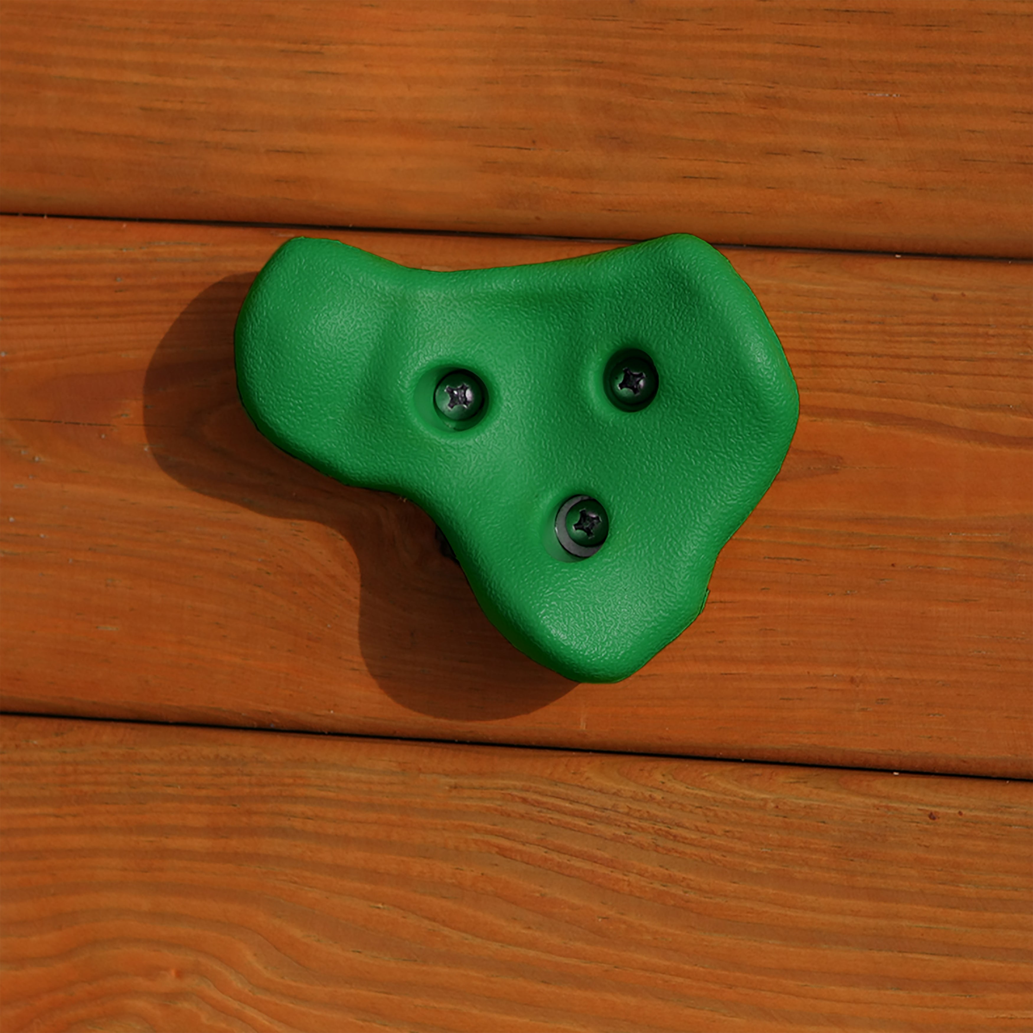 Green textured climbing hold with three screws mounted on wooden playset panel for outdoor climbing walls