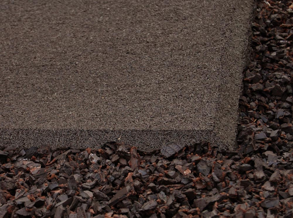 Earthtone recycled rubber playground mat with beveled edge surrounded by dark mulch beneath playground equipment