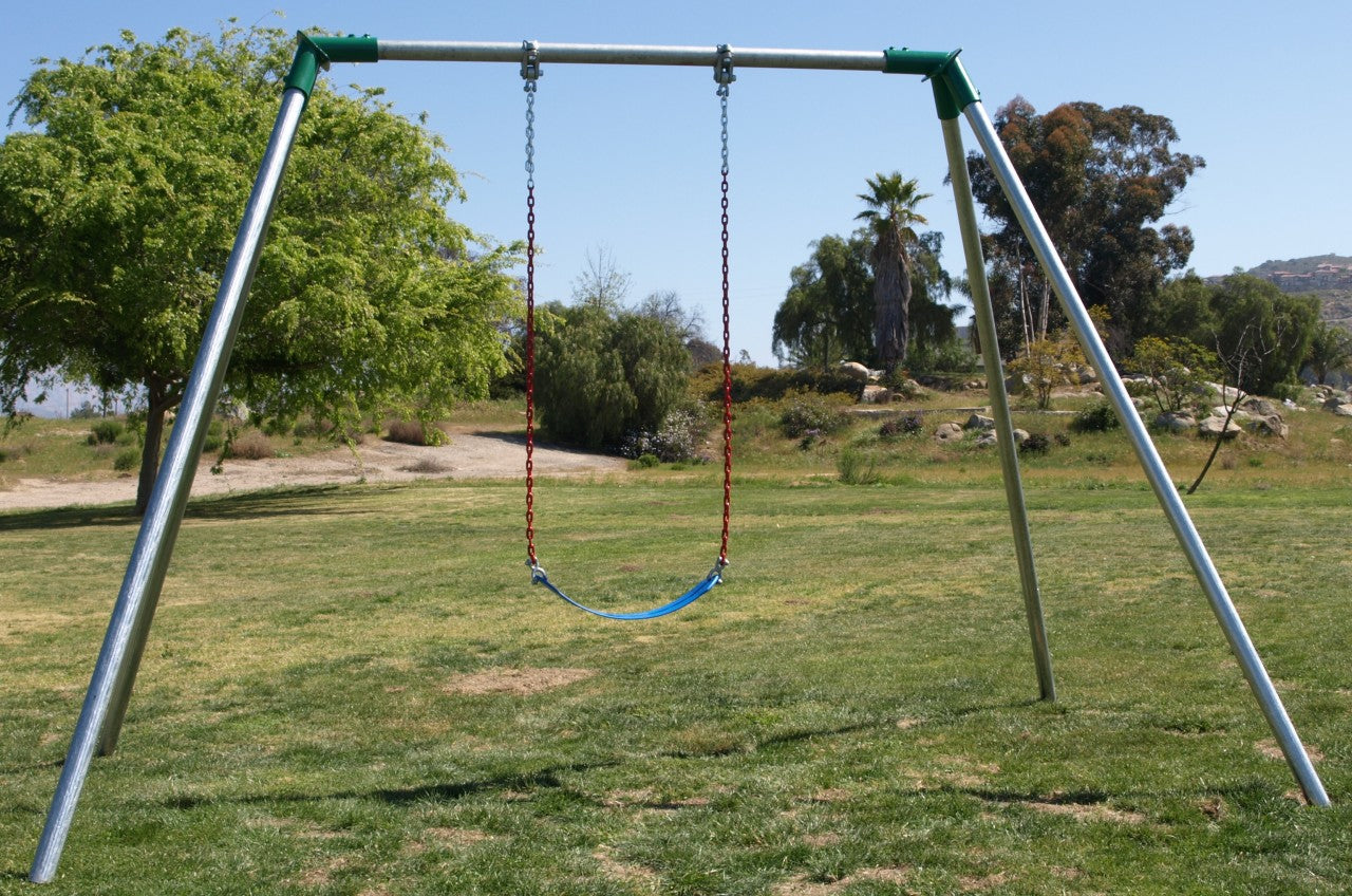Metal swing set frame with single blue seat suspended by red chains on grassy playground