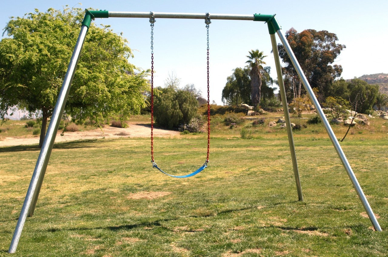 Single-bay metal swing set with blue seat and red chains on grassy field with trees and hills in background