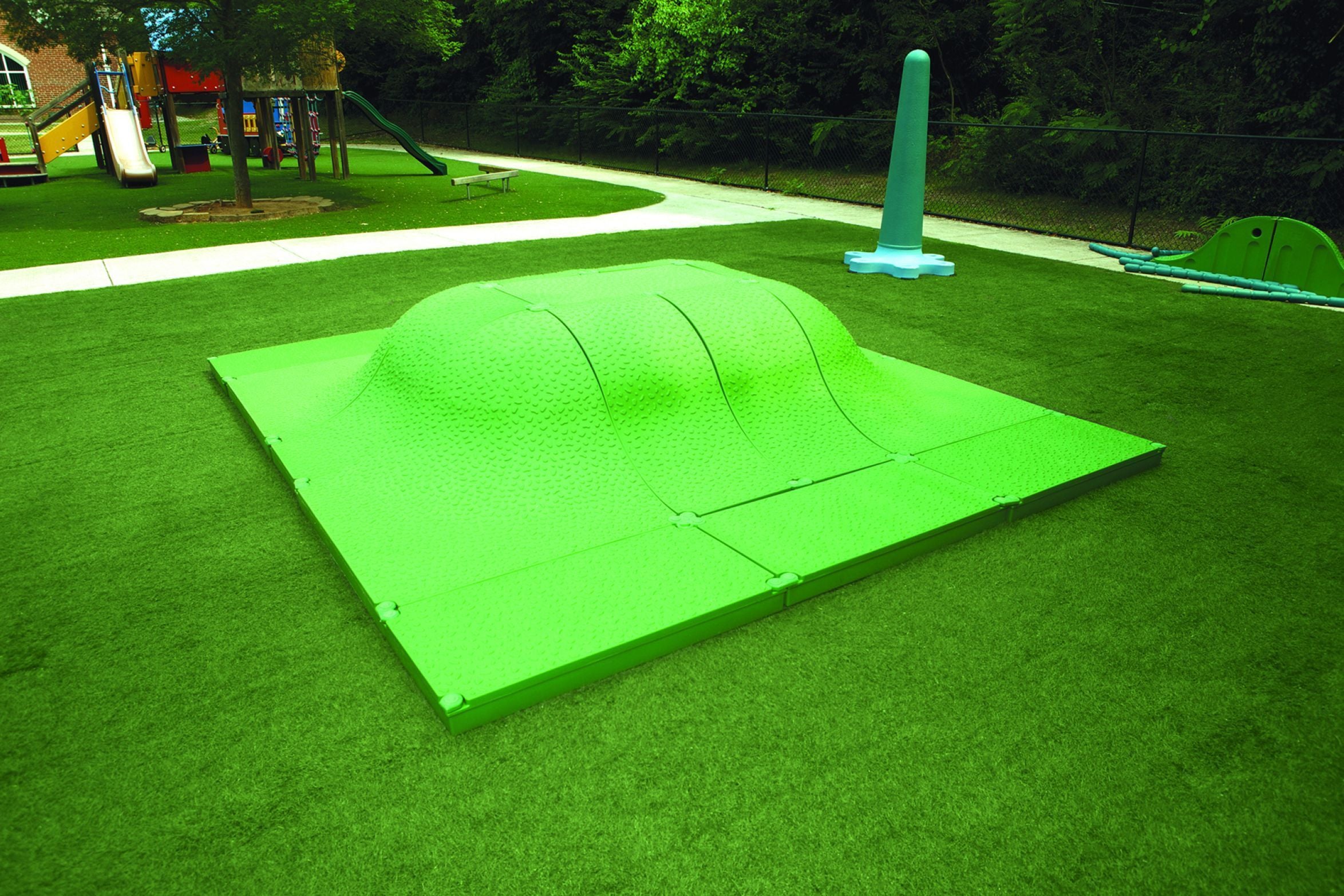 Green textured play mound with gentle slopes on artificial turf in an outdoor playground setting