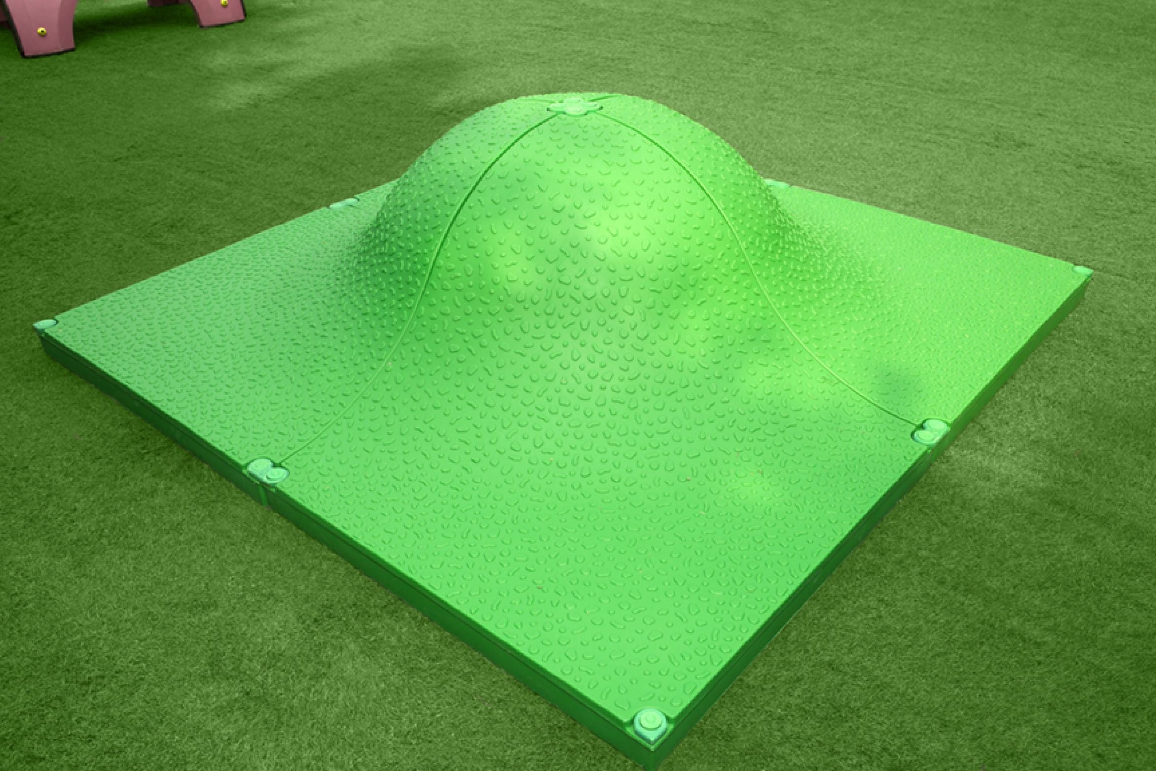 Green textured modular play mound with rounded peak on artificial grass, designed for interactive outdoor play and exploration