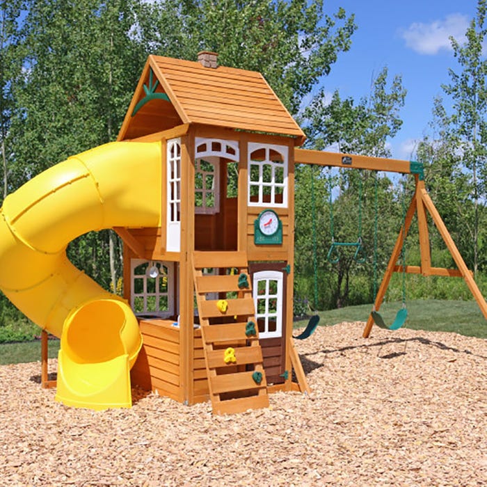 Creston Lodge Wooden Swing Set with two-level clubhouse, multicolored climbing rockwall, yellow twist tube slide, dual belt swings, and play kitchen on wood chip ground