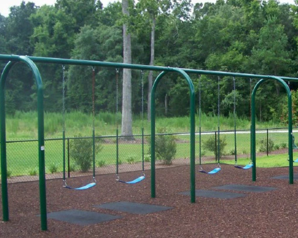Playground swing set with green metal frame, blue plastic seats, and black rubber safety mats on loose fill surfacing