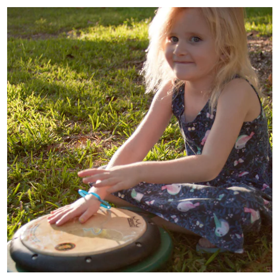Child playing outdoors on colorful single drum table with tunable REMO drum-heads, surrounded by grass