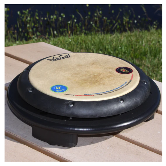 Tunable REMO drum-head mounted on a black plastic base, outdoor setting with grass, percussion instrument for rhythm play.
