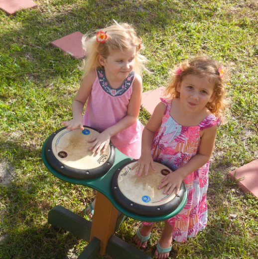 Two young girls playing on a green double drum table with mallet-friendly heads outdoors on grass