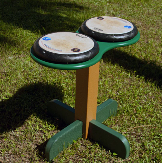 Outdoor musical drum table with two hand-playable drum pads on a sturdy green and brown base set on grass