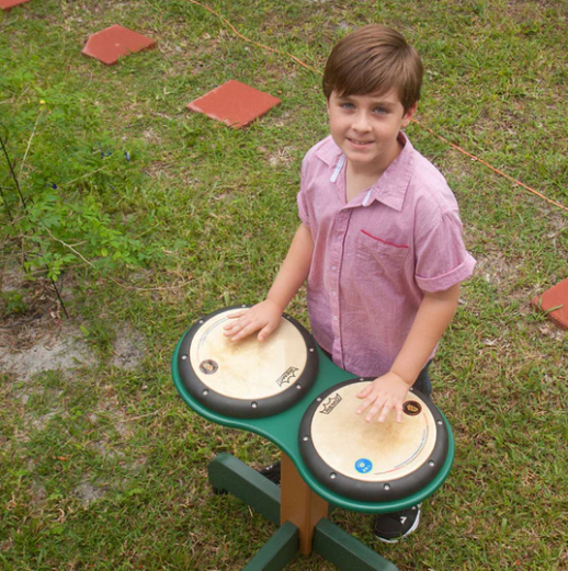 Overhead view of a child playing a green double drum table with natural drum heads on grass