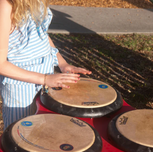 Outdoor musical drum table with three professional drum pads and a child playing rhythms on hand- and mallet-friendly surfaces