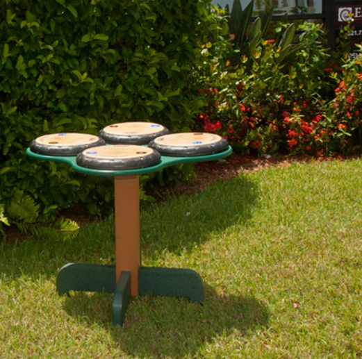 Outdoor drum table with four professional drum heads on green and brown stand surrounded by grass and plants