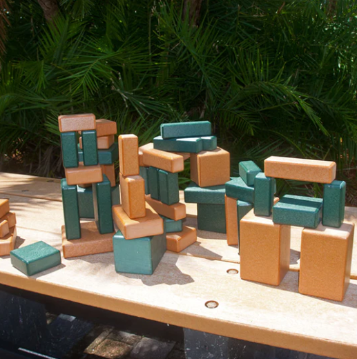 Stacked eco-friendly green and tan recycled plastic building blocks outdoors with natural foliage backdrop