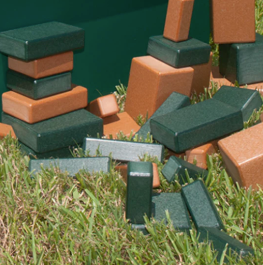 Stacked and scattered durable green and brown recycled plastic building blocks in various shapes on grass for creative play