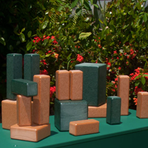 Green and brown eco-friendly building blocks arranged on a green surface with surrounding foliage and red flowers