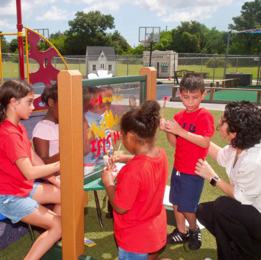 Children painting on a clear double-sided recycled plastic art easel outdoors with adult supervision