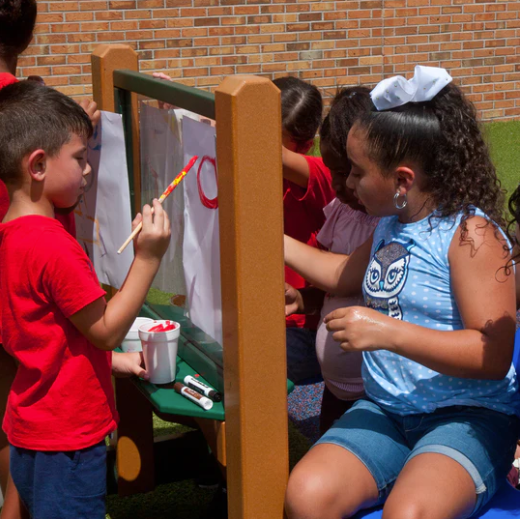 Children painting on a double-sided clear recycled plastic art easel outdoors with colorful brushes and markers